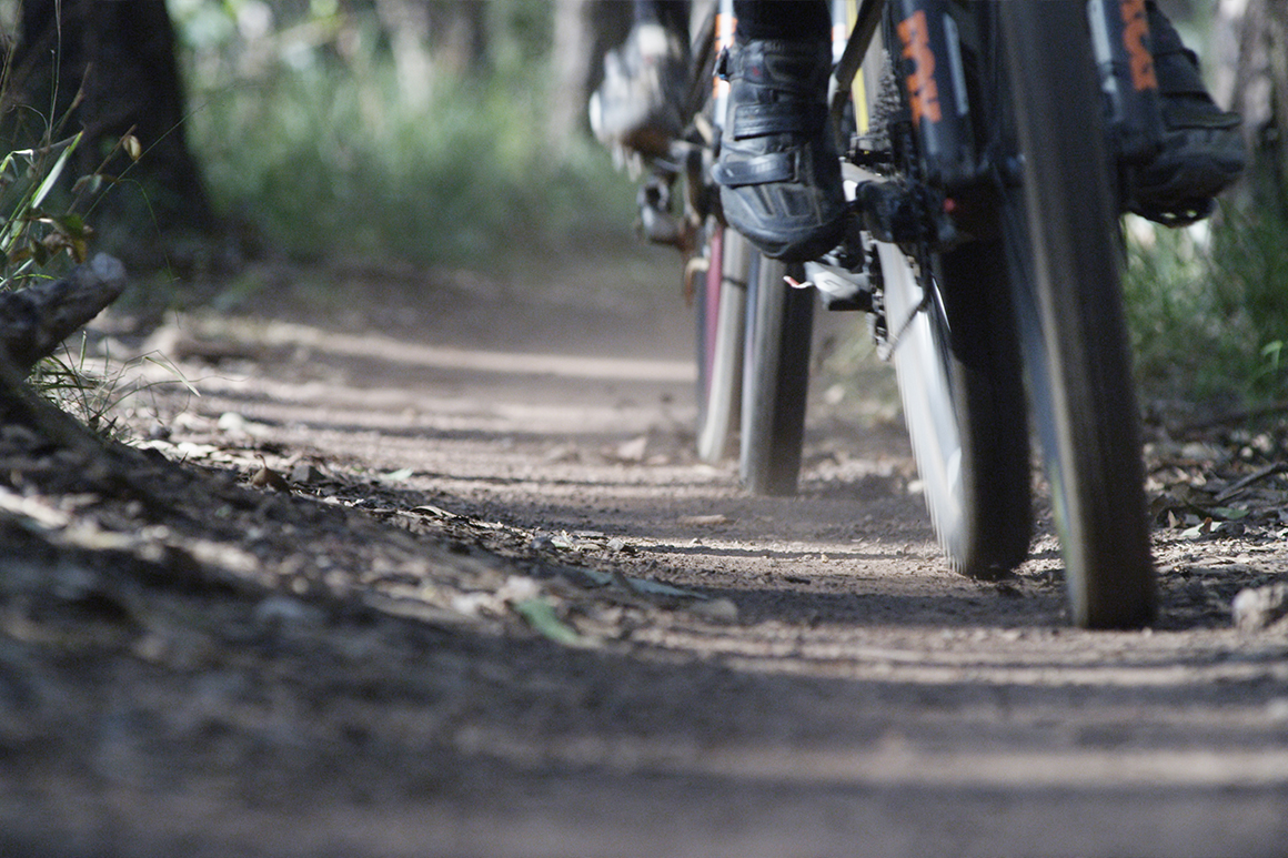 A close-up of wheels and mountain biking shoes as two riders traverse along a dirt path.