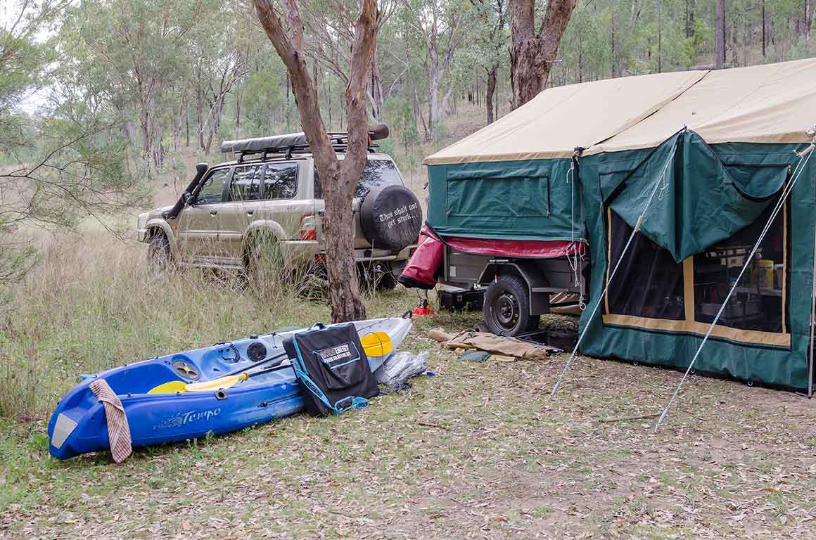 Camper trailer, tent, canoe and 4-wheel-drive vehicle parked at bush campsite.
