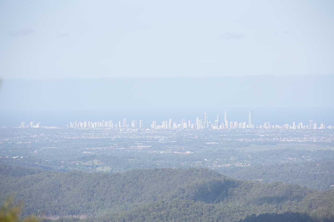 Distant skyline of skyscrapers of the Gold Coast with ocean in background and forested hills in foreground.