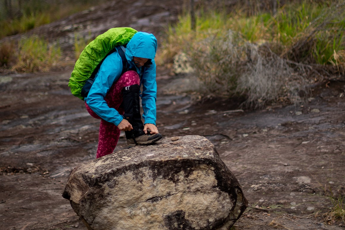 Person with pack and rain jacket adjusts boot on a rock. 