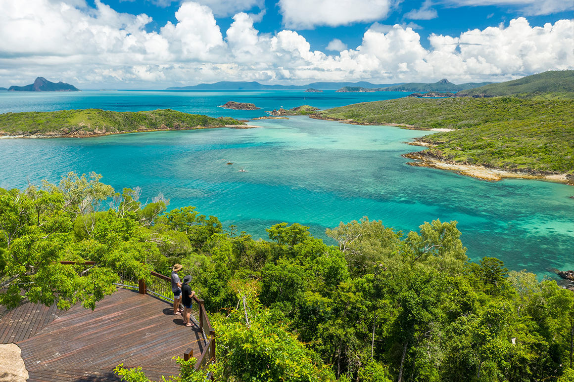 Scenic view from lookout over sand, ocean and distant islands clad in lush vegetation.