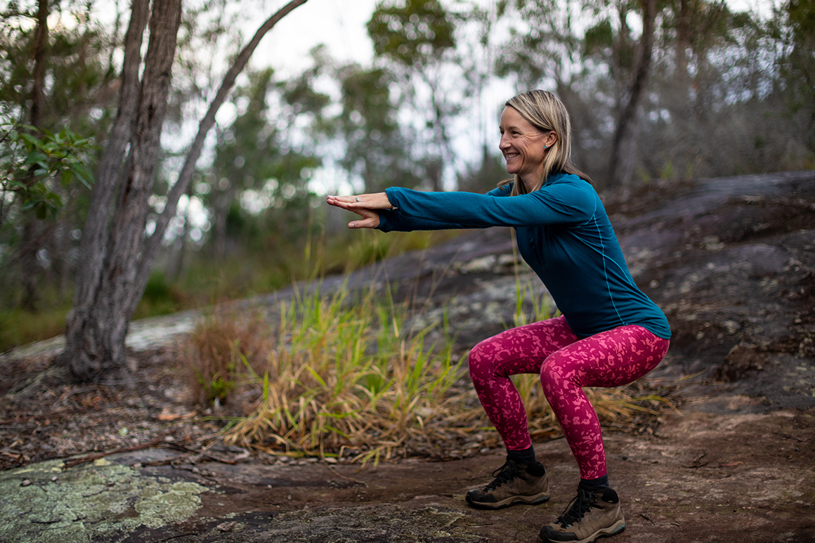 A female hiker in pink and blue active wear is squatting on a rocky walking track. 