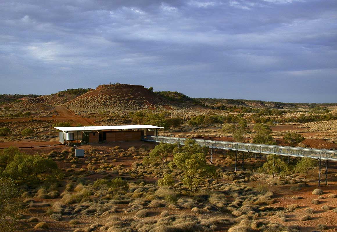 Solar powered building and long walkway nestled in an expansive savanna landscape dotted with spinifex.