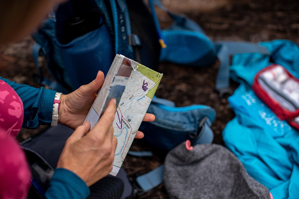 A folded park map with walking tacks is being opened by a hiker. 