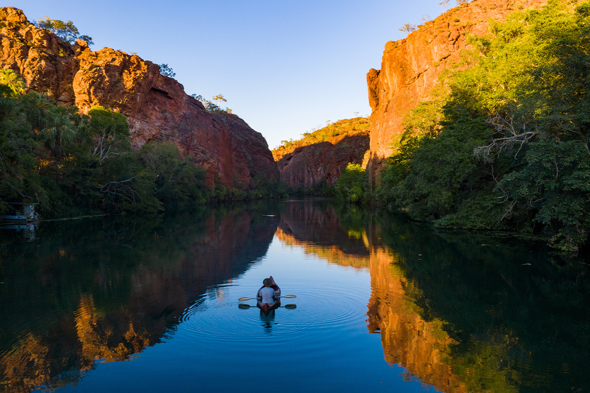 A canoe glides up a creek framed by tall sandstone gorge walls.