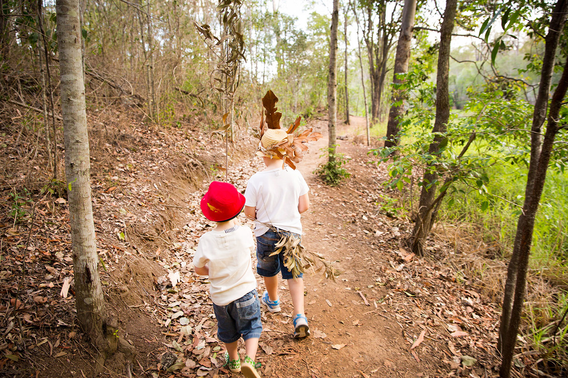 Two young children with hats walking along track with open forest each side of the track