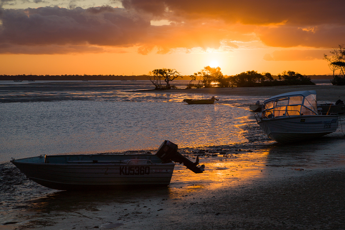 Golden sunset colours the shallow waters of the bay and tow tinnies resting high and dry in the shore. 